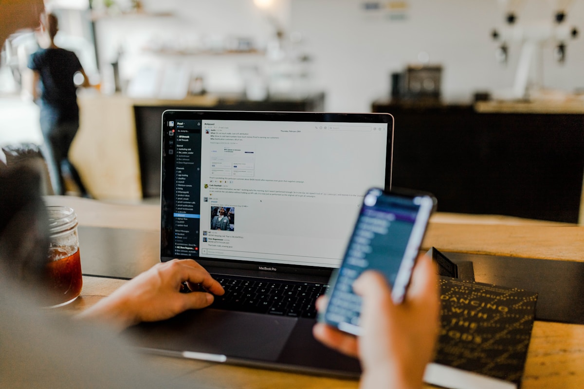 A person using an app on a phone while working at a laptop